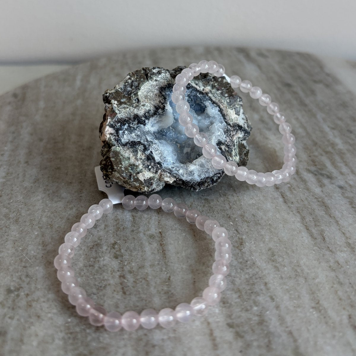 Rozenkwarts kinderarmband liggend voor een geode op marmer
