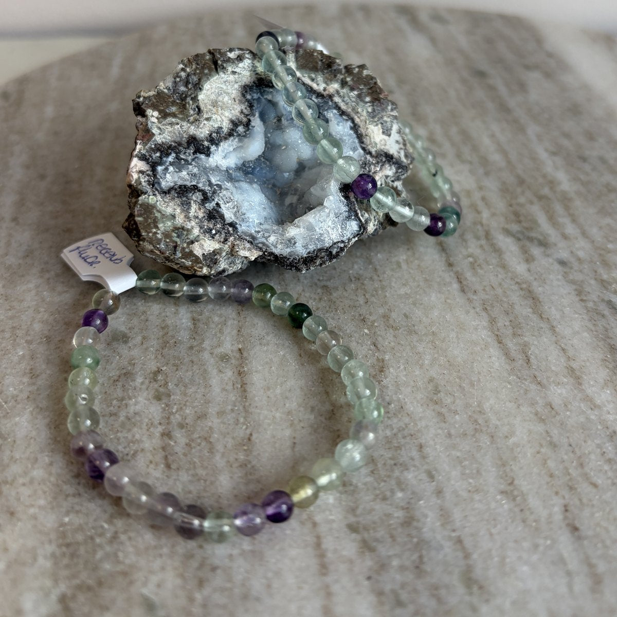 Regenboog fluoriet kinderarmband liggend voor een geode op marmer