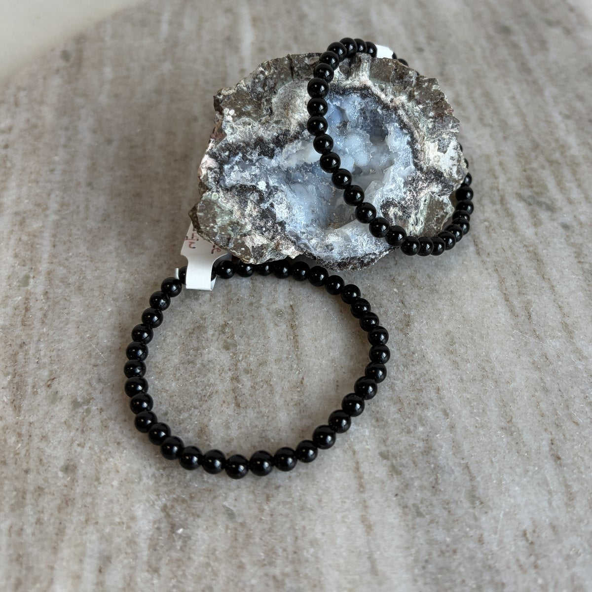 Zwarte toermalijn kinderarmband liggend voor een geode op marmer